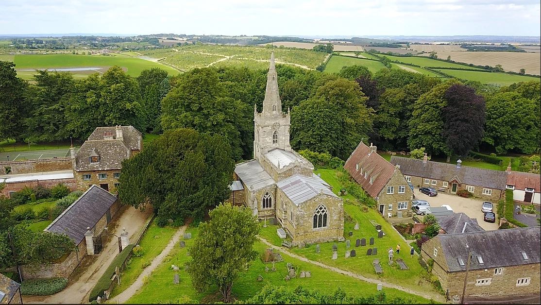 Aerial view of church with steeple, with churchyard, houses and far views