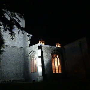 A church at night, surrounded by trees but with warm light showing through the windows