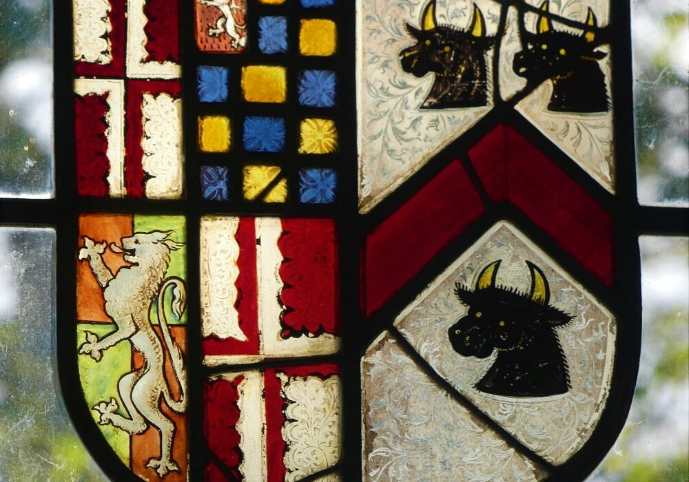 A shield shaped panel of stained glass showing a coat of arms of three bulls head arranged around a red chevron