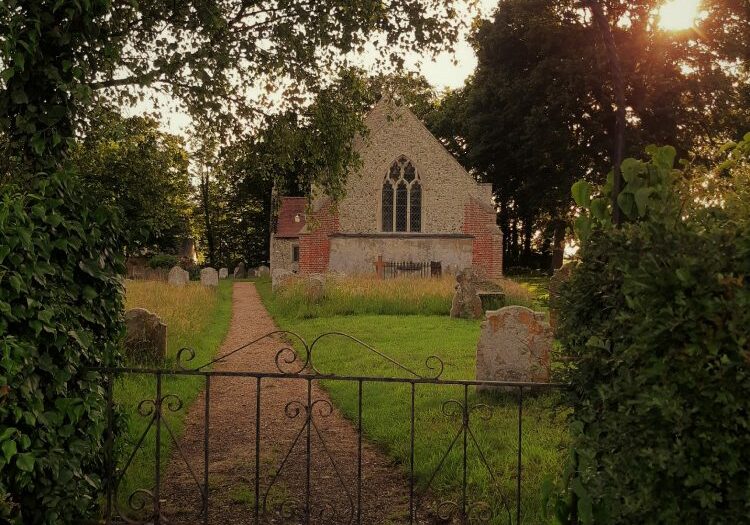 An iron gate and arched gateway, the end of church is just visible through the gate