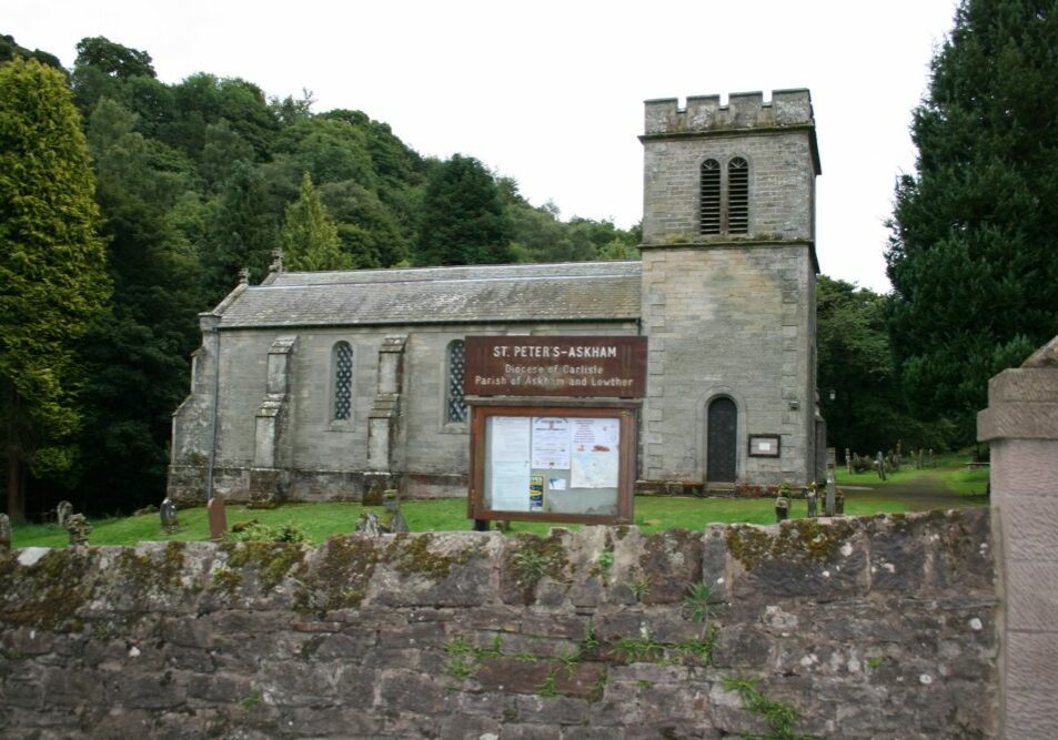 Church with bell tower, surrounded by trees, with sign and a few people in churchyard