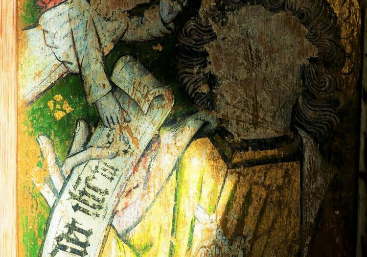 ChurchImages Norfolk Foulden Rood Screen Small A close up of the firgure of a saint, lit by yellow sunlight. The saint carries a scroll and his face has been scratched out