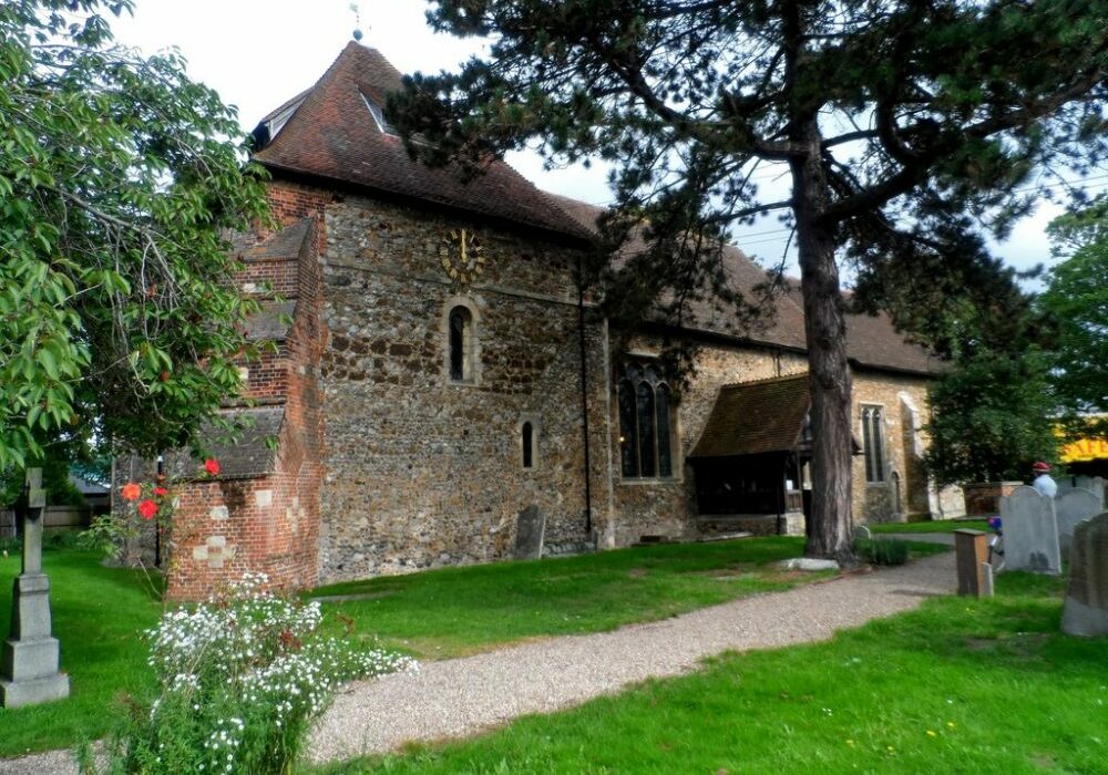 The exterior of a small flint church with a tiled roof and a clock
