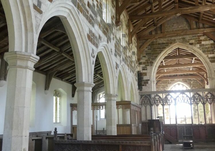 A tell sunlit church, the pillars are white stone and the walls are patchwork of white, red, brown and green stone