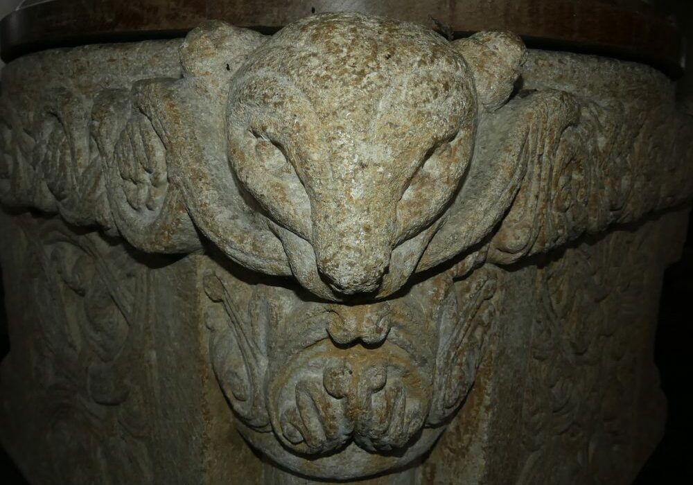 The corner of a square, Norman font carved with a stylised animals head looking directly at the camera