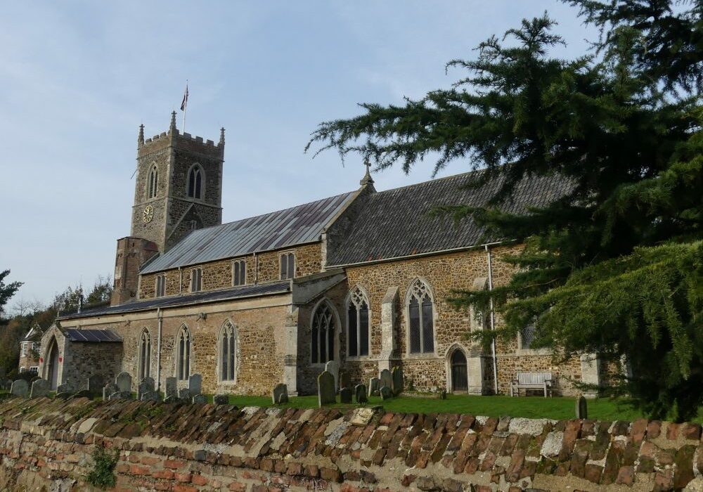 ChurchImages Norfolk Watlington Ext Exterior of a long, low looking church made of gingerbread coloured stone surrounded by a brick wall
