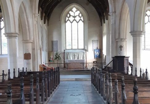 ChurchImages-Norfolk Wood Dalling Interior A font at the font of the photo, then a view up the aisle of a church to a clear glass window