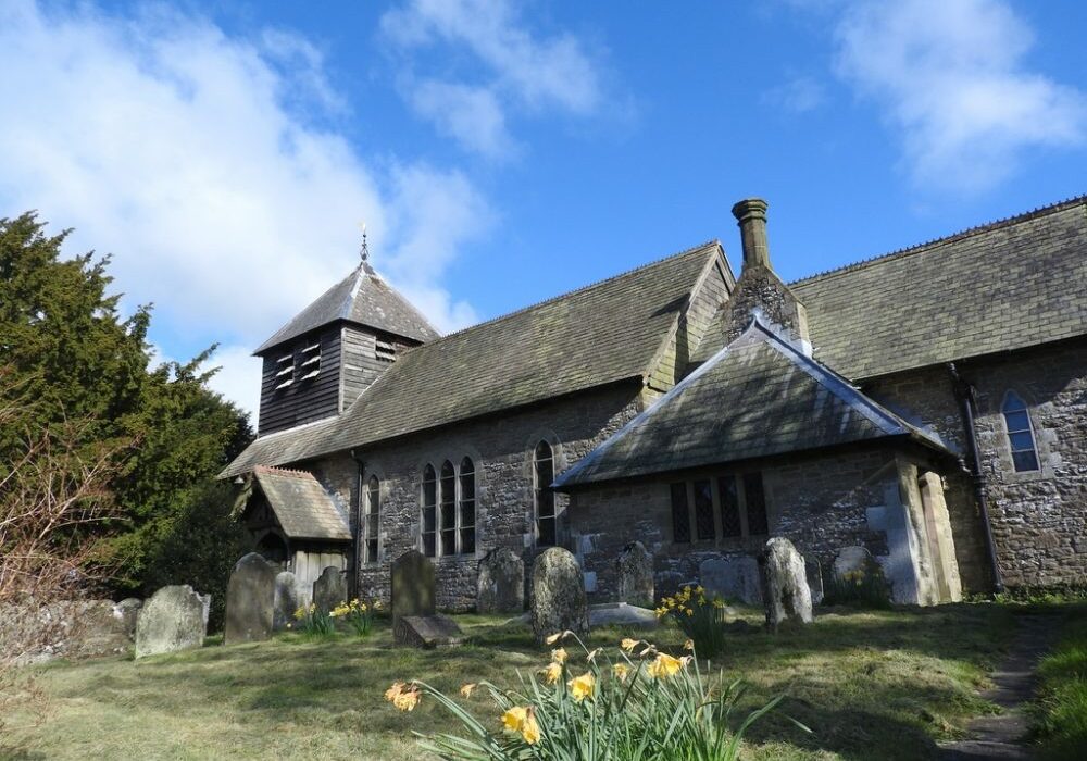 St Michael, Wentnor, Shropshire exterior Old stone church with wooden belfry and daffodils in churchyard